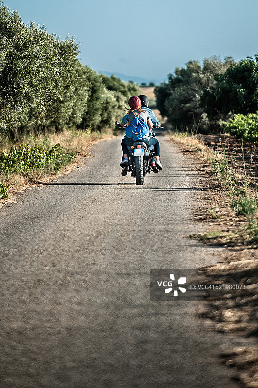 中年夫妇在意大利撒丁岛卡利亚里乡村道路上骑摩托车的背影图片素材
