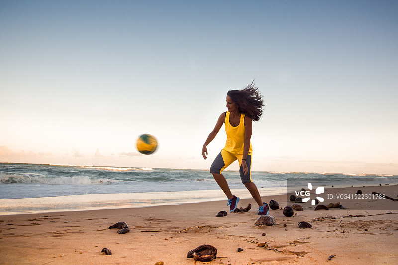 在日落时分踢沙滩足球的年轻巴西女人图片素材