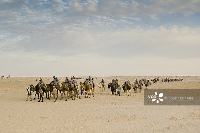 在绿洲附近沙漠中骑骆驼的游客图片素材