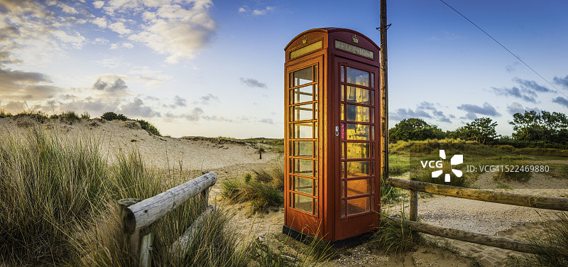 海滨日出时照亮的英国红色电话亭图片素材