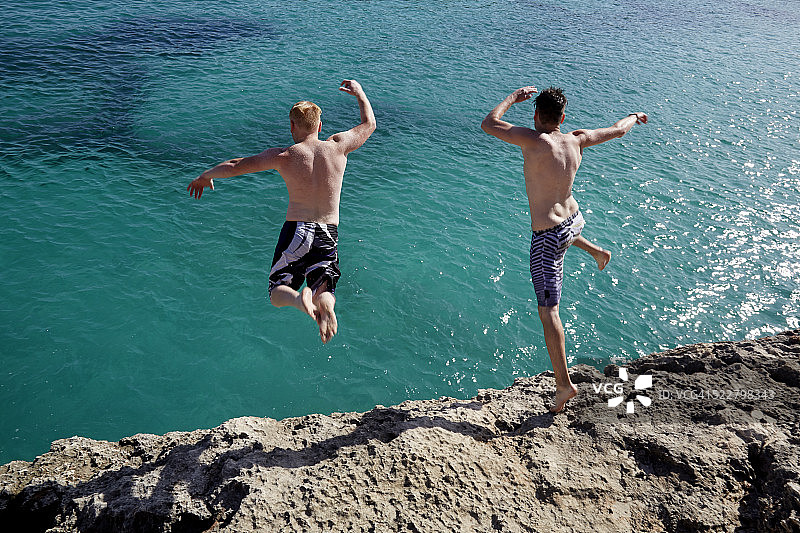 年轻男子从岩石跳入蓝色大海图片素材