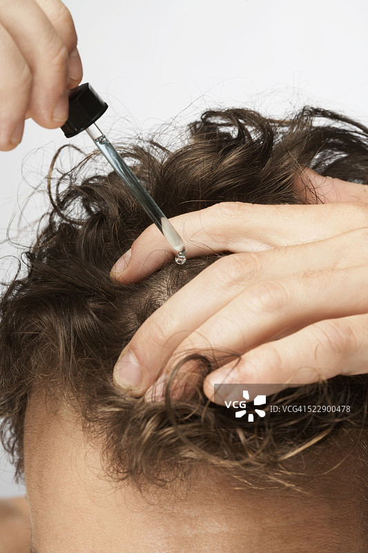 男人将精华液滴在头发上图片素材