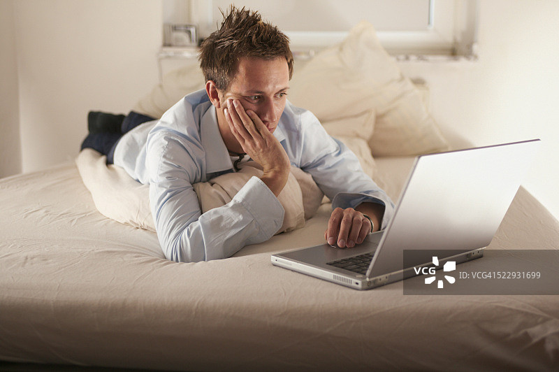 年轻男人躺在床上用笔记本电脑图片素材