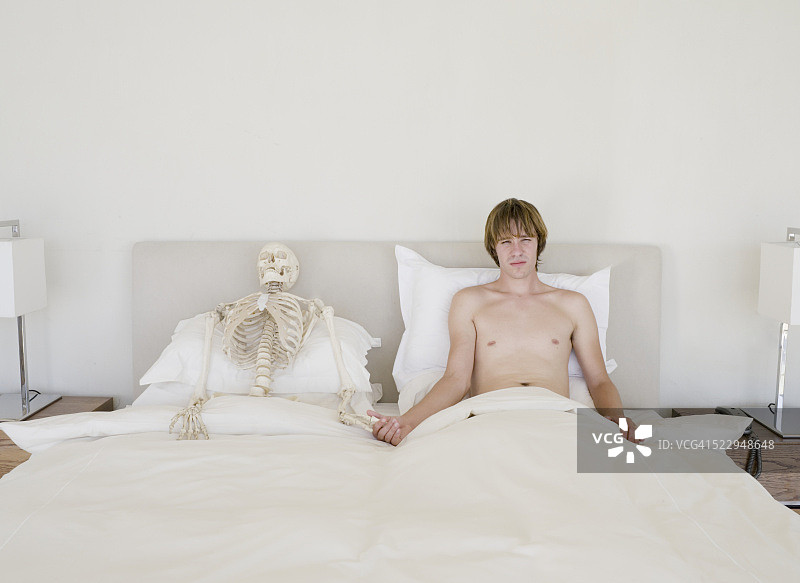 男人躺在骷髅旁边的床上图片素材