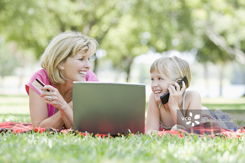 女子和女孩在公园里使用笔记本电脑和手机图片素材