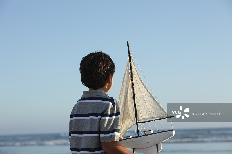 男孩（7-9岁）拿着玩具帆船看着大海图片素材
