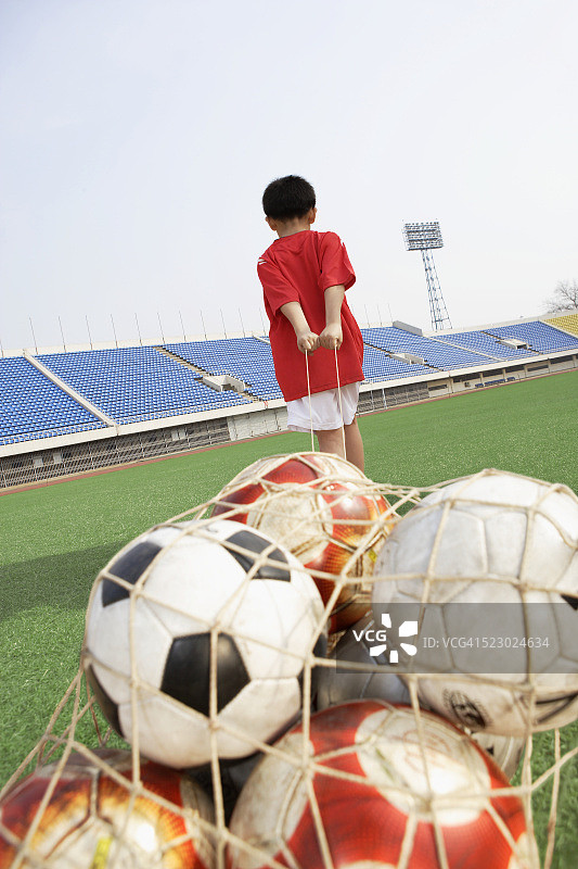 男孩拖着一袋足球图片素材