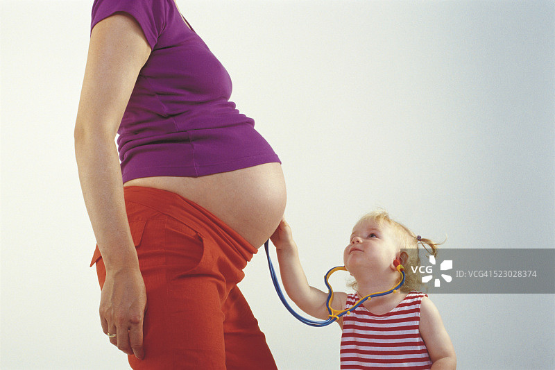 幼儿拿着听诊器贴在怀孕母亲的肚子上图片素材