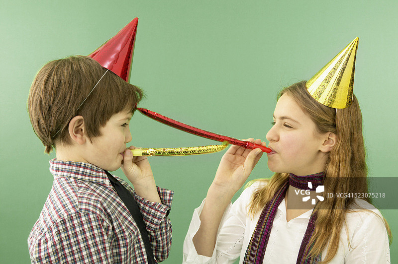 戴着派对帽的男孩和女孩吹着响亮的玩具图片素材