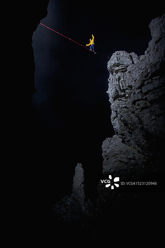 男子在奥地利蒂罗尔的夜间，于两块岩石之间的高空绳索上保持平衡图片素材