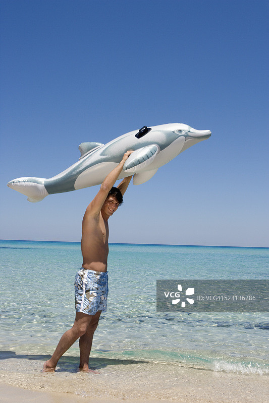 在海滩上拿着玩具海豚的年轻男人图片素材