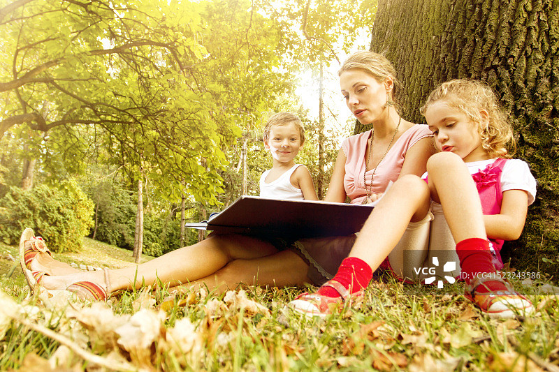 年轻母亲和两个孩子一起阅读图片素材