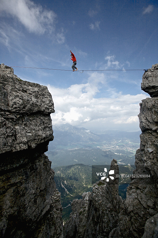 男人在奥地利蒂罗尔山区两座悬崖之间的高空绳索上保持平衡图片素材