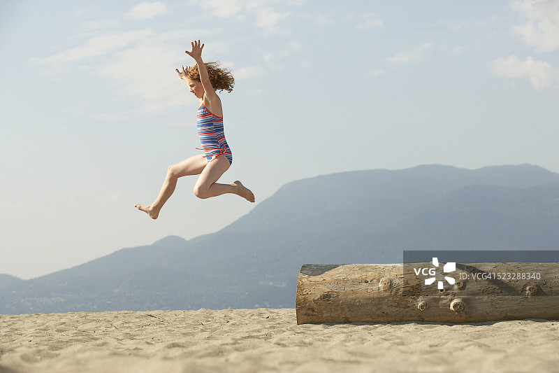 在海滩上从圆木上跳下来的女孩图片素材