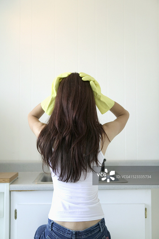 戴着橡胶手套站在厨房里的年轻女人图片素材