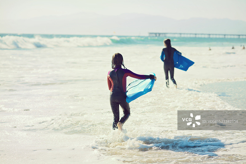 两个穿着潜水服的女孩拿着趴板走向大海图片素材