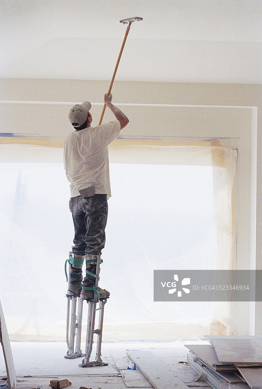 工人在装修房间内踩着高跷打磨天花板图片素材