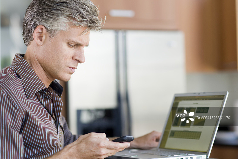 男人在厨房使用笔记本电脑和手机图片素材