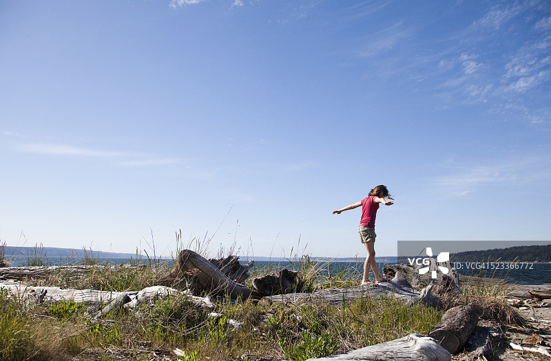女孩在海滩上漂木上保持平衡图片素材