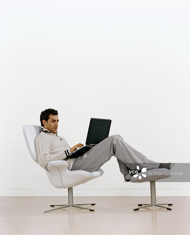 男人躺在椅子上使用笔记本电脑图片素材