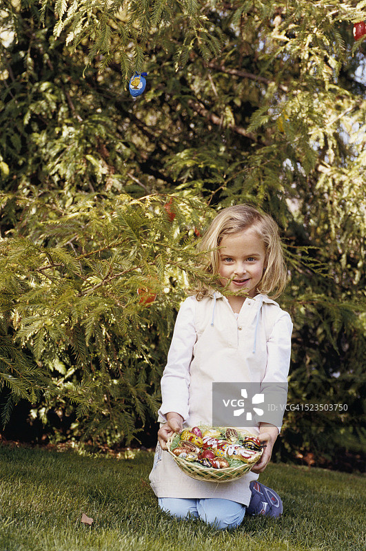 在草坪上拿着装有复活节糖果的篮子的金发女孩图片素材