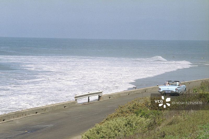 女性驾驶复古福特雷鸟跑车沿海岸线行驶图片素材