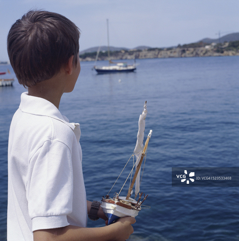 拿着玩具船看着帆船的男孩图片素材