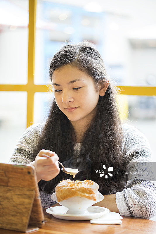 迷人的女孩边吃热午餐边看平板电脑图片素材