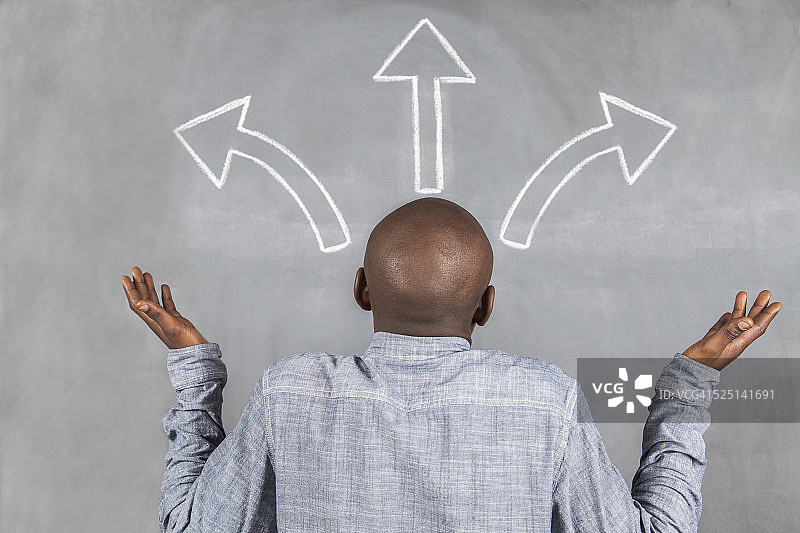 男人面对画有箭头的黑色黑板图片素材