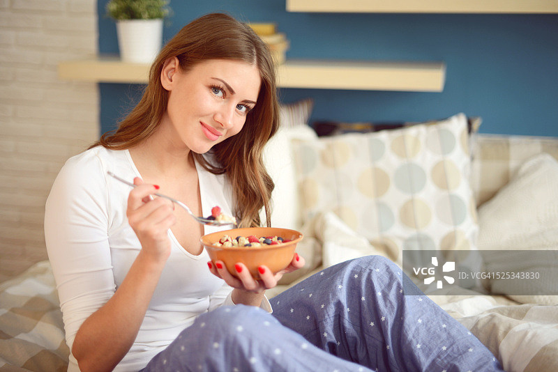 在卧室里穿着睡衣吃什锦早餐和浆果的女人图片素材