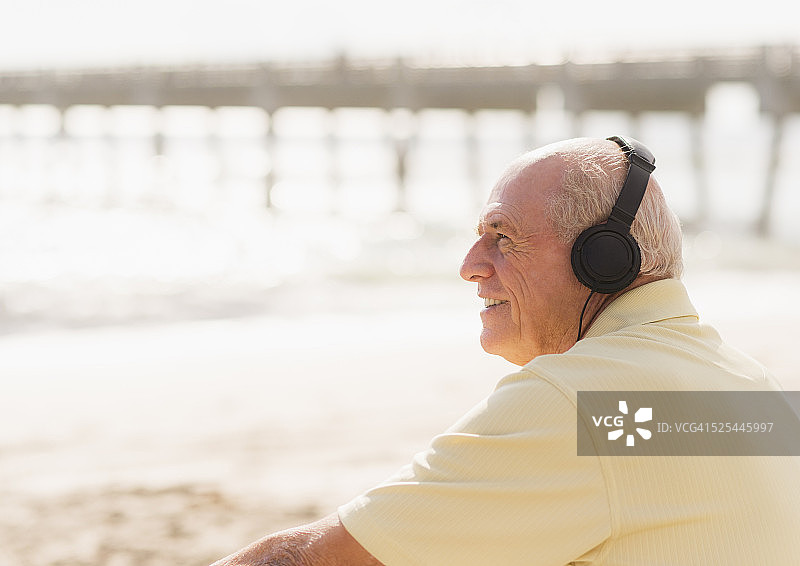 美国佛罗里达州朱庇特：戴着耳机坐在海滩上的老年男人图片素材
