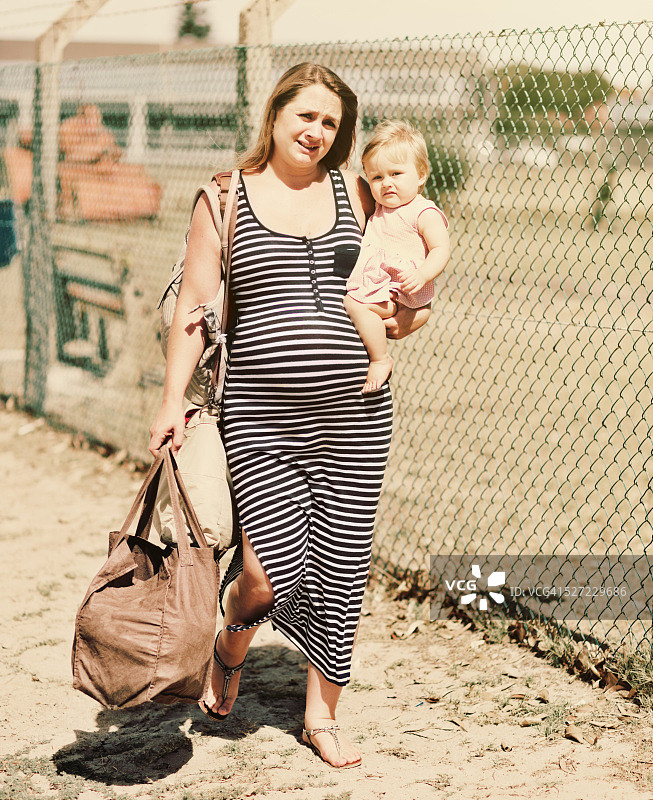 孕妇带着蹒跚学步的孩子穿过贫困地区，感到沮丧和疲惫图片素材