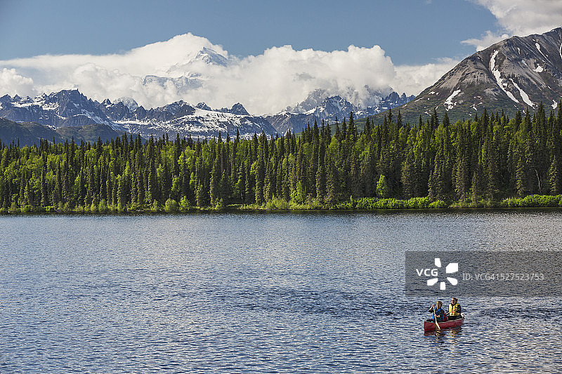 德纳里州立公园(Denali State Park),拜尔斯湖(Byers lake)上,两名妇女和一个年轻女孩在红色的独木舟上。拜尔斯湖的海岸线绿树成荫,德纳利山(Mount McKinley)在云雾中高耸图片素材