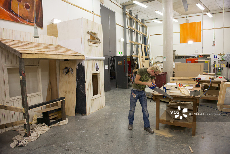 在工作室锯木头的年轻木匠图片素材