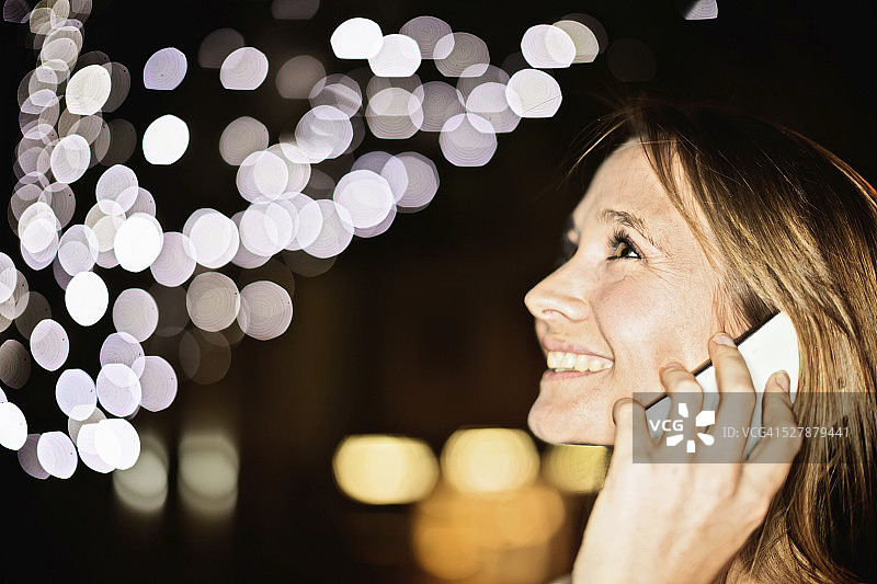 美丽的女人使用手机，脸上闪烁着失焦的灯光图片素材