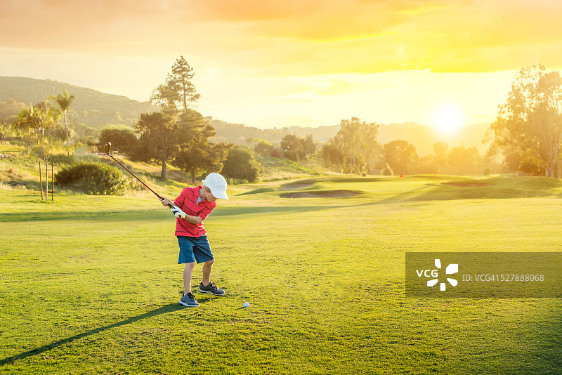日落时挥杆的高尔夫球小男孩图片素材