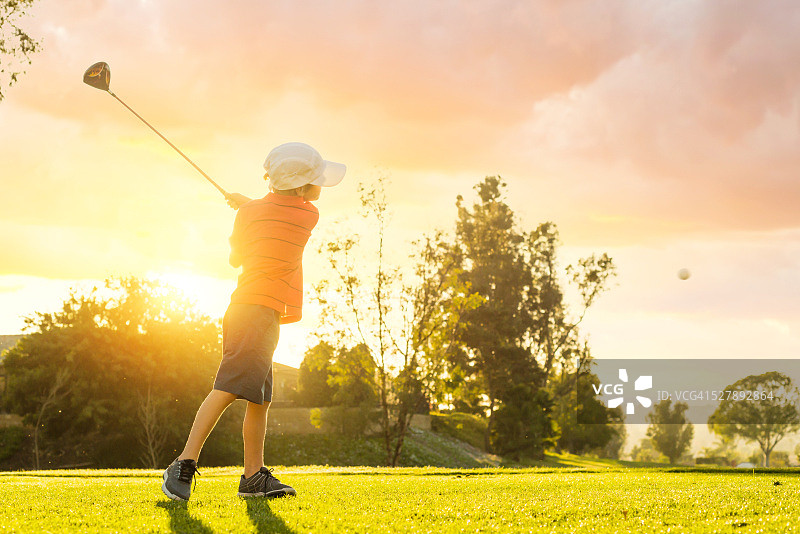 日落时挥杆的高尔夫球小男孩图片素材