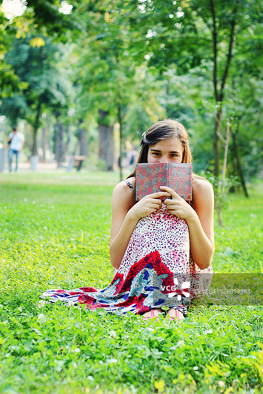 在草地上用书遮住脸的女孩图片素材