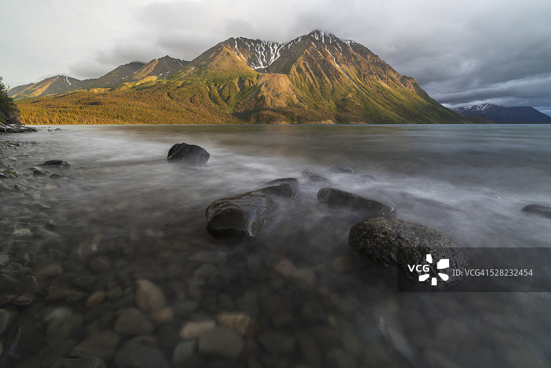 加拿大育空地区克卢恩国家公园，夕阳照射国王宝座，凯瑟琳湖水冲击岩石的长曝光图片素材