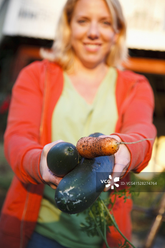一位妇女拿着花园里的新鲜蔬菜；美国华盛顿州芬代尔图片素材