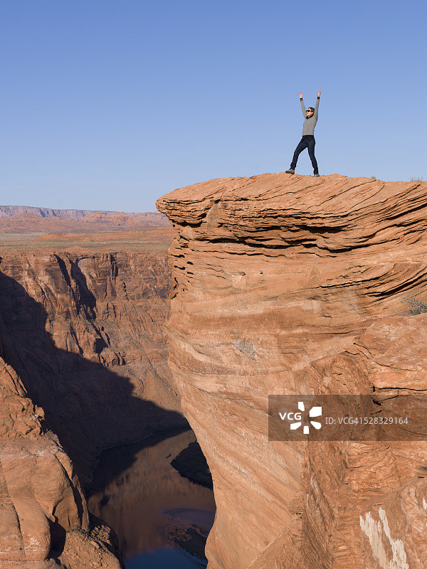 站在岩石悬崖边举起双臂的女人；美国亚利桑那州马蹄湾图片素材