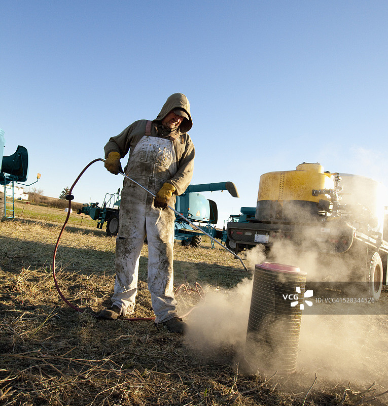 男子清洁农用设备；加拿大阿尔伯塔省的三座山图片素材