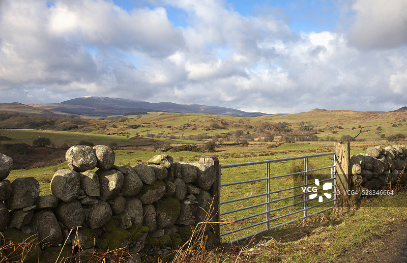石墙上的金属门与丘陵景观；苏格兰邓弗里斯图片素材
