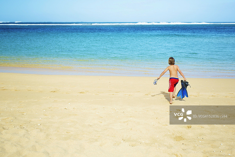 男孩在海滩上奔向大海，带着浮潜装备；考艾岛，夏威夷，美国图片素材