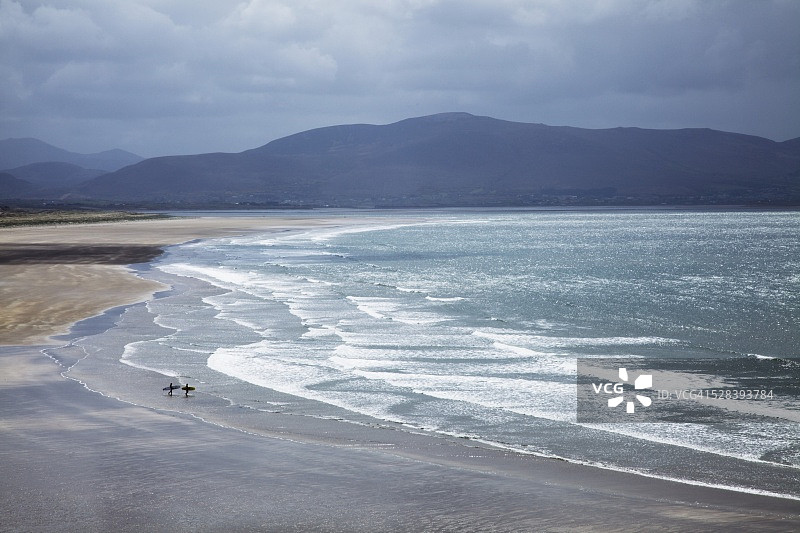 两人在丁格尔半岛因奇海滩上拿着冲浪板散步；爱尔兰凯里郡图片素材