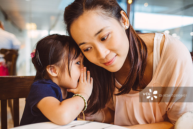 在咖啡馆里对着妈妈耳语的小孩图片素材
