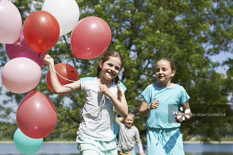 女孩们在公园里拿着气球奔跑（德国巴伐利亚慕尼黑卡尔斯费尔德湖）图片素材