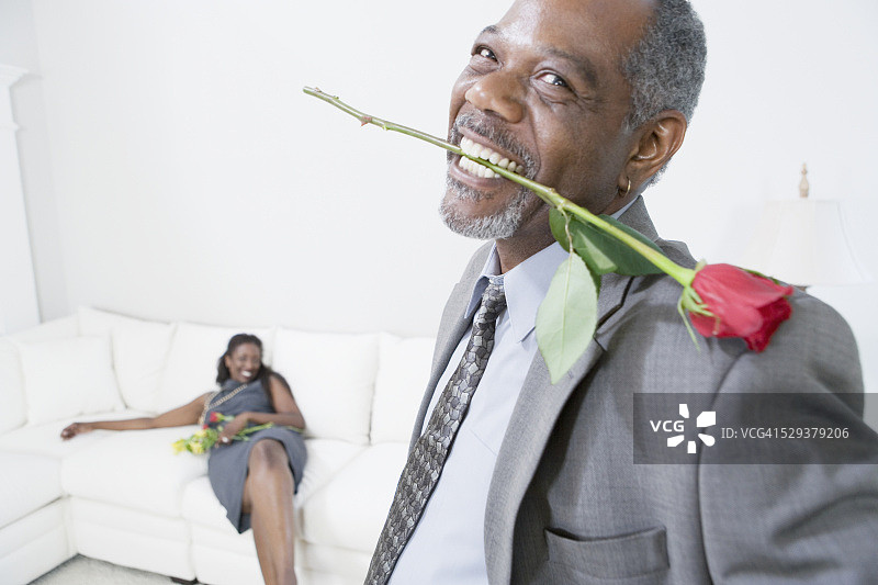 男人嘴叼玫瑰，妻子在背景图片素材