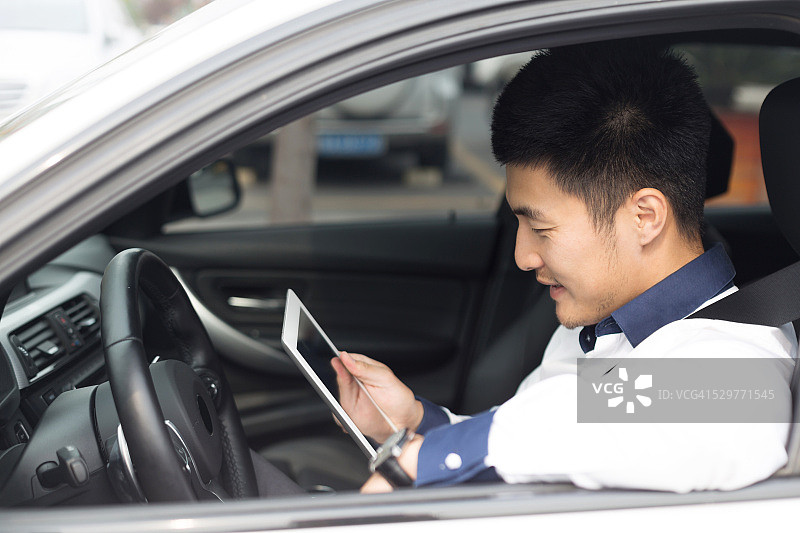 在车里使用智能平板电脑的亚洲年轻男商人图片素材
