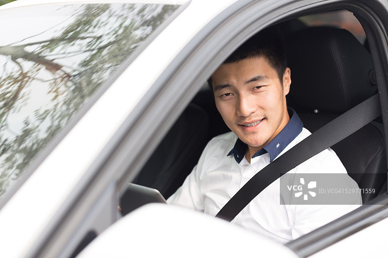 在车里使用智能平板电脑的亚洲年轻男商人图片素材